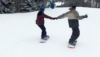 snow boarders holding hands going down trail